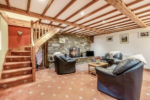 Un salon chaleureux avec une cheminée en pierre, des canapés en cuir et un escalier en bois.