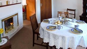 A dining room with a round table set for four, surrounded by chairs. A fireplace is visible to the left, and a wooden door leads to another room. - Loningside (Wolverhampton)