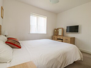Un dormitorio con cama, cómoda, televisor y ventana con persianas.