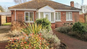 A two-story brick house with a tiled roof, white-framed windows, and a front garden with various plants.