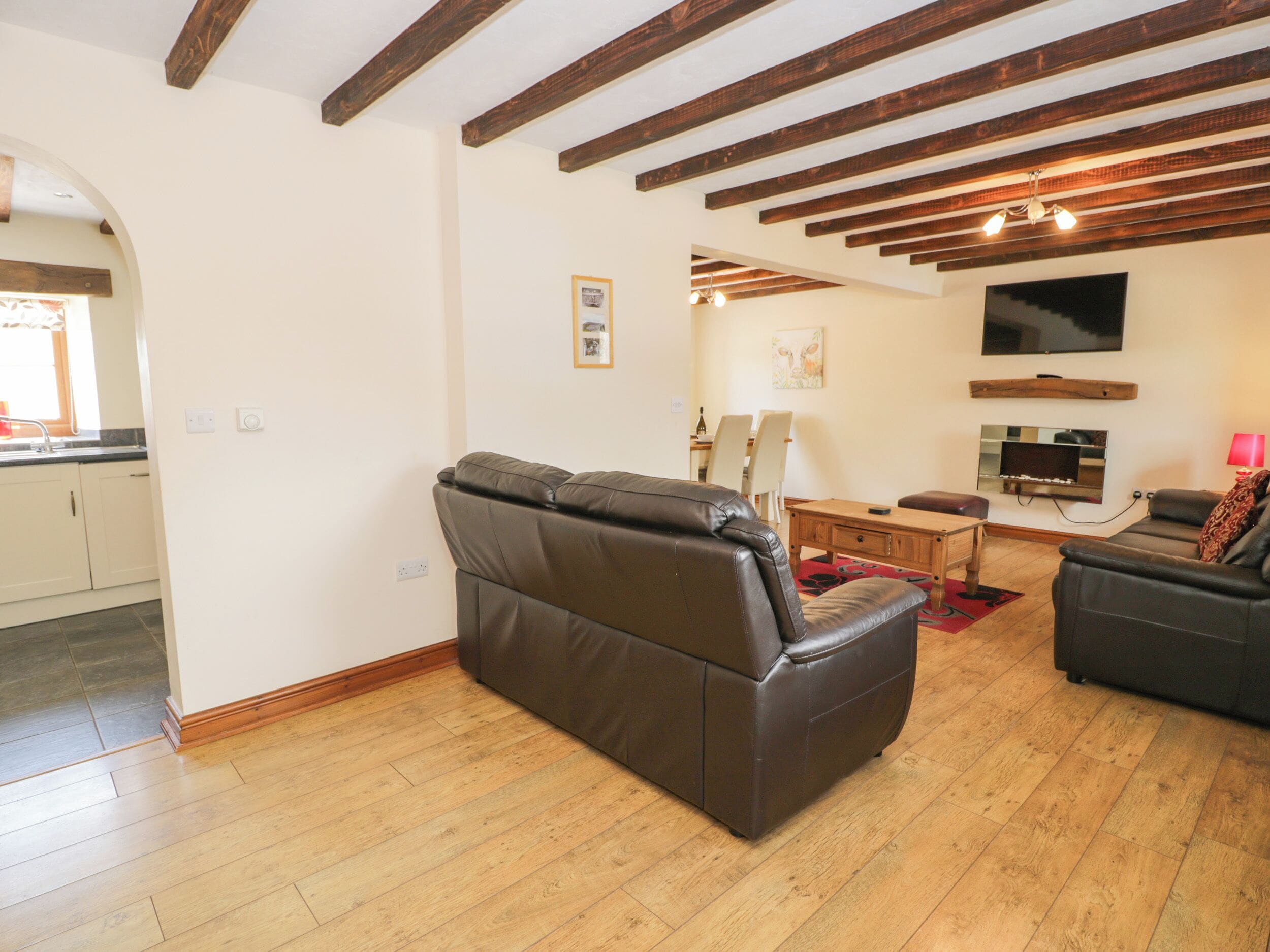 A living room with a brown leather sofa, a wooden dining table, and a flat-screen TV mounted on the wall.