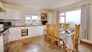 A kitchen with white cabinets, a microwave, and a dining table with chairs. - Pen Y Gaer (Denbigh)