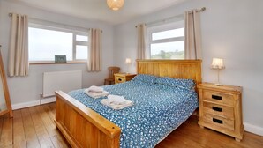 A bedroom with a wooden bed, two bedside tables, a window with curtains, and a radiator. - Pen Y Gaer (Denbigh)