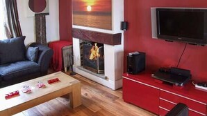 Una sala de estar con chimenea, un sofá, una mesa de centro y un televisor montado en la pared.
