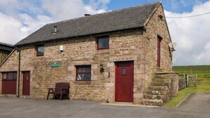 A stone building with a red door and windows, a bench outside, and a green sign on the wall. - Downsdale Cottage (Buxton)