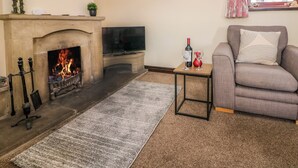 A living room with a fireplace, a television, a sofa, and a small table with a bottle and glasses. - Downsdale Cottage (Buxton)