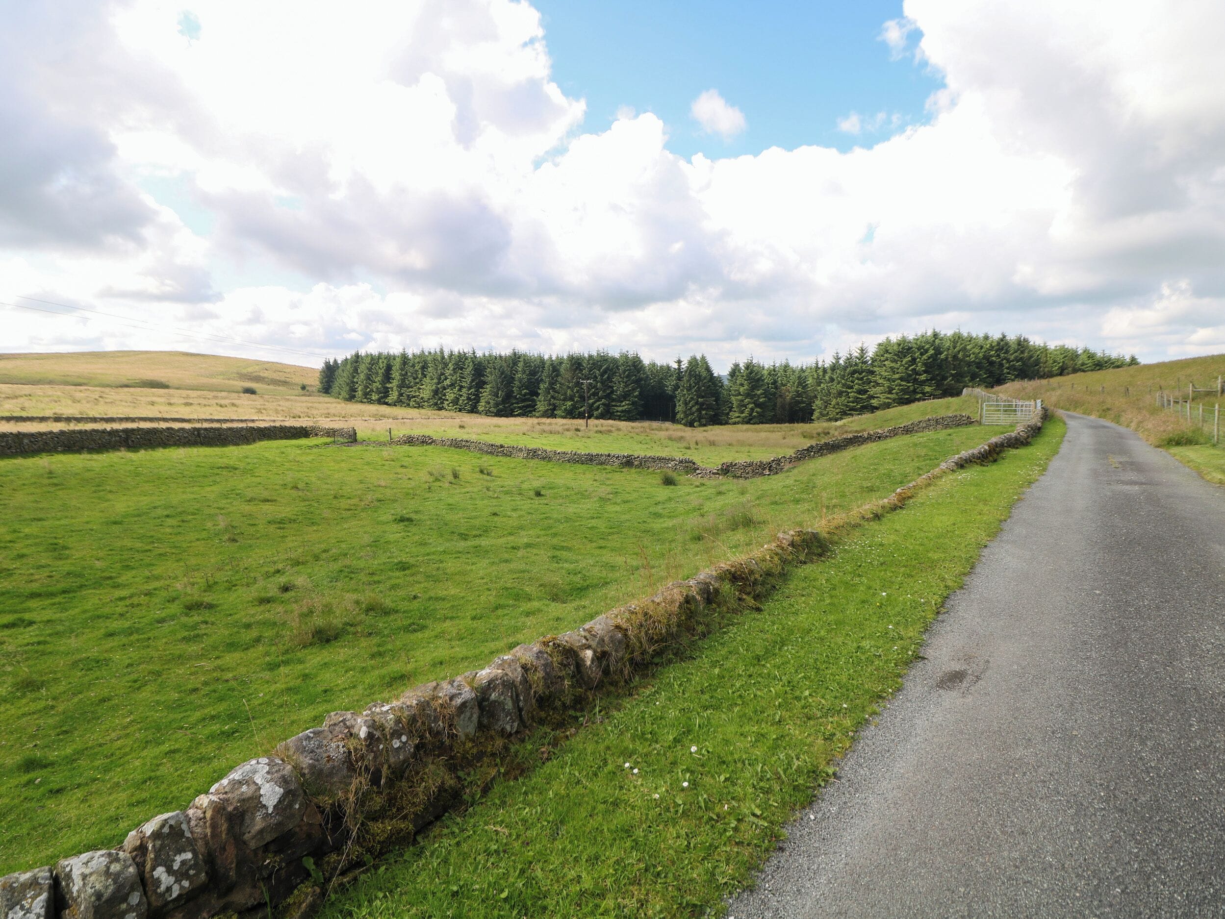 A rural road flanked by stone walls and green fields.