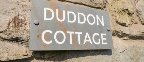A sign on a stone wall that reads "DUDDON COTTAGE".