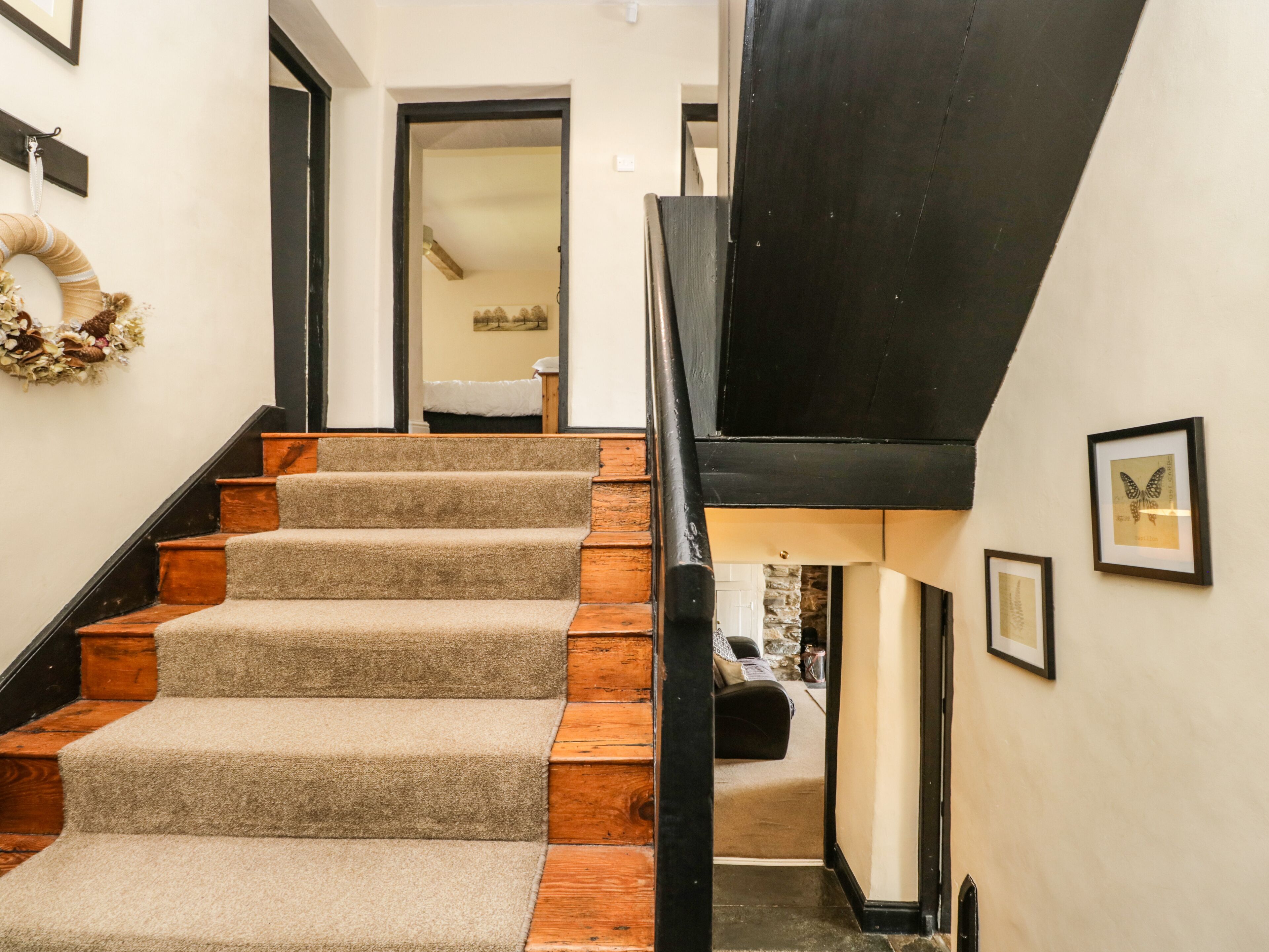 Un escalier dont les marches sont recouvertes de moquette et les contremarches en bois, menant à un palier du deuxième étage agrémenté d’une rambarde noire.