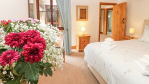 A bedroom with a bed, bedside tables, a mirror, and a window with curtains. - Riddings Barn (Kendal)
