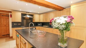 A kitchen with wooden cabinets, a stainless steel sink, and a vase of flowers on the counter. - Riddings Barn (Kendal)