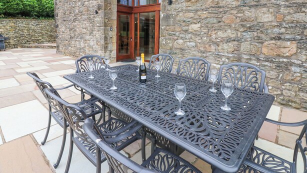 A stone building with a large patio table set for six, surrounded by chairs. - Riddings Barn (Kendal)