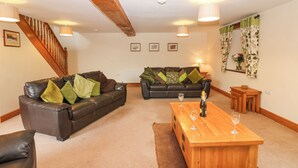 A spacious living room with two leather sofas, a wooden coffee table, and a staircase with wooden railings. - Riddings Barn (Kendal)