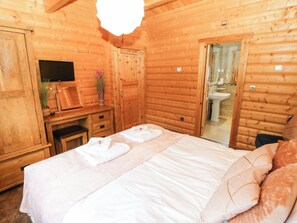 A wooden cabin room with a bed, a TV, a mirror, and a bathroom visible through an open door. - Cornfield (Northallerton)