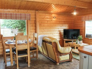 A cozy cabin interior with a wooden interior, a sofa, a television, and a dining area with a table and chairs. - Cornfield (Northallerton)