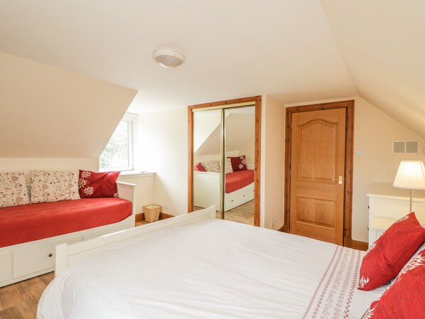 A bedroom with a large bed, a wardrobe, a mirror, and a window. - 10 Monarch Country Apartments (Newtonmore)