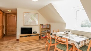 A dining area with a table and chairs, a bookshelf, a television, and a map on the wall. - 10 Monarch Country Apartments (Newtonmore)