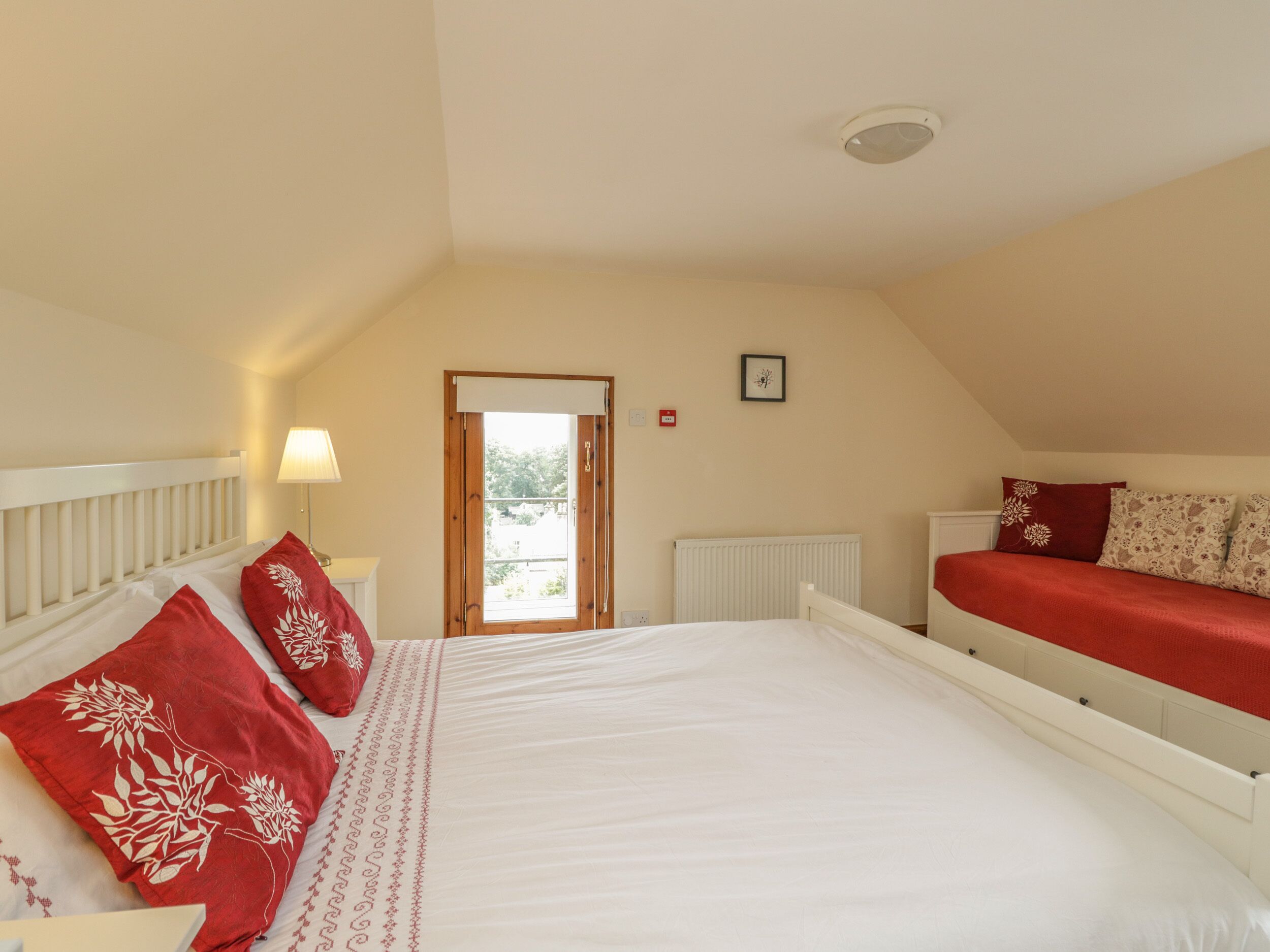 A bedroom with a large bed, a smaller bed, a window, a radiator, and a door.