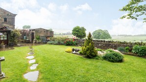 A rustic stone building with a garden pathway leading to a wooden door. - Green Clough Farm (Bradford)