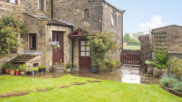 A stone building with a traditional design, featuring a front entrance with a wooden door and a small porch area. - Green Clough Farm (Bradford)
