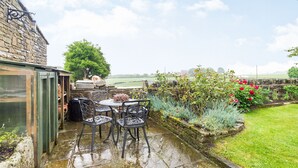 A patio with a table and chairs, a stone wall, and a view of the countryside. - Green Clough Farm (Bradford)