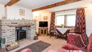 A cozy living room with a stone fireplace, wooden beams, a television, a dining table with chairs, and a red sofa. - Green Clough Farm (Bradford)