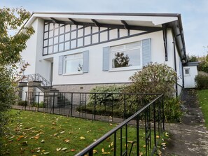A modern two-story house with a white exterior and blue shutters, a front garden with a metal fence, and a staircase leading to the entrance. - Silverdale Mount (Grange-over-Sands)