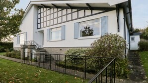 Una casa moderna de dos plantas con fachada blanca, contraventanas azules y base de piedra.