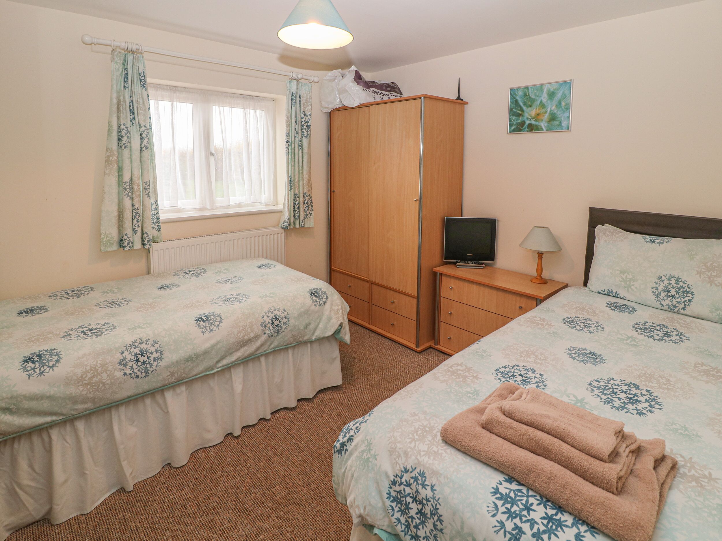 A bedroom with two beds, a wardrobe, a television, and a lamp.