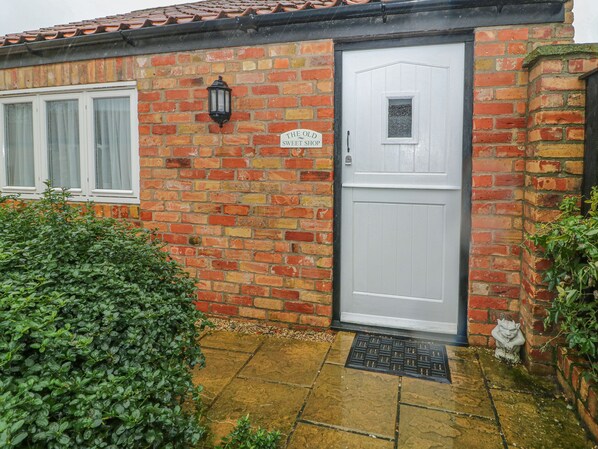 A brick house with a white door, a small window, and a sign that reads "The Old Sweet Shop". - Old Sweet Shop (Louth)