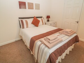 A neatly made bed with a striped blanket and folded towels, a bedside table with a lamp, and a door in the background. - Old Sweet Shop (Louth)