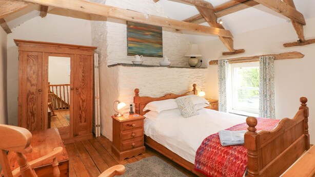 Een slaapkamer met een houten bed, een nachtkastje, een houten stoel, een bureau, een raam met gordijnen en een trap.