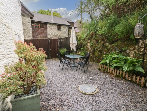 A patio area with a table and chairs, surrounded by a stone wall and greenery. - Bwthyn Y Felin Star (Llanfyrnach)