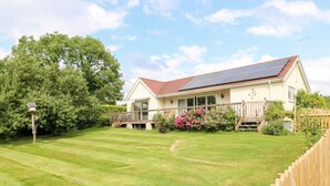 A house with a solar panel roof, a wooden deck, and a well-maintained lawn. - Clovermead Cottage (Derby)