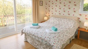 A bedroom with a large bed, a balcony, floral wallpaper, and a wooden floor. - Clovermead Cottage (Derby)