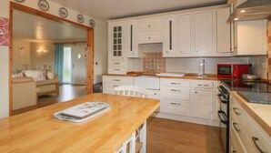 A compact kitchen with white cabinets, a wooden countertop, and a red microwave. - Clovermead Cottage (Derby)