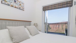 A bedroom with a large bed, a headboard, a painting on the wall, and a window with a view of the outside. - Waddleduck (Whitby)