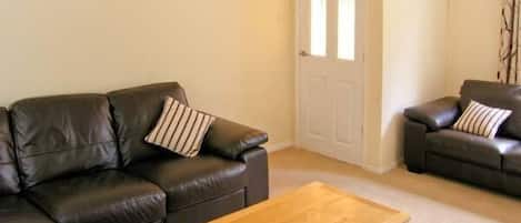 A living room with a brown leather sofa, a wooden coffee table, and a white door.