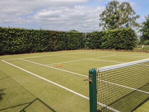 Una cancha de tenis con una red, rodeada por un seto.