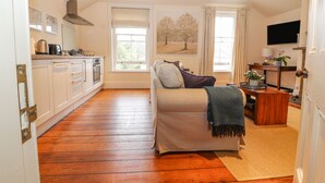 A spacious living area with a sofa, a coffee table, and a TV. There is a kitchen area with cabinets and a stove. - Cook's Flat (Wrexham)