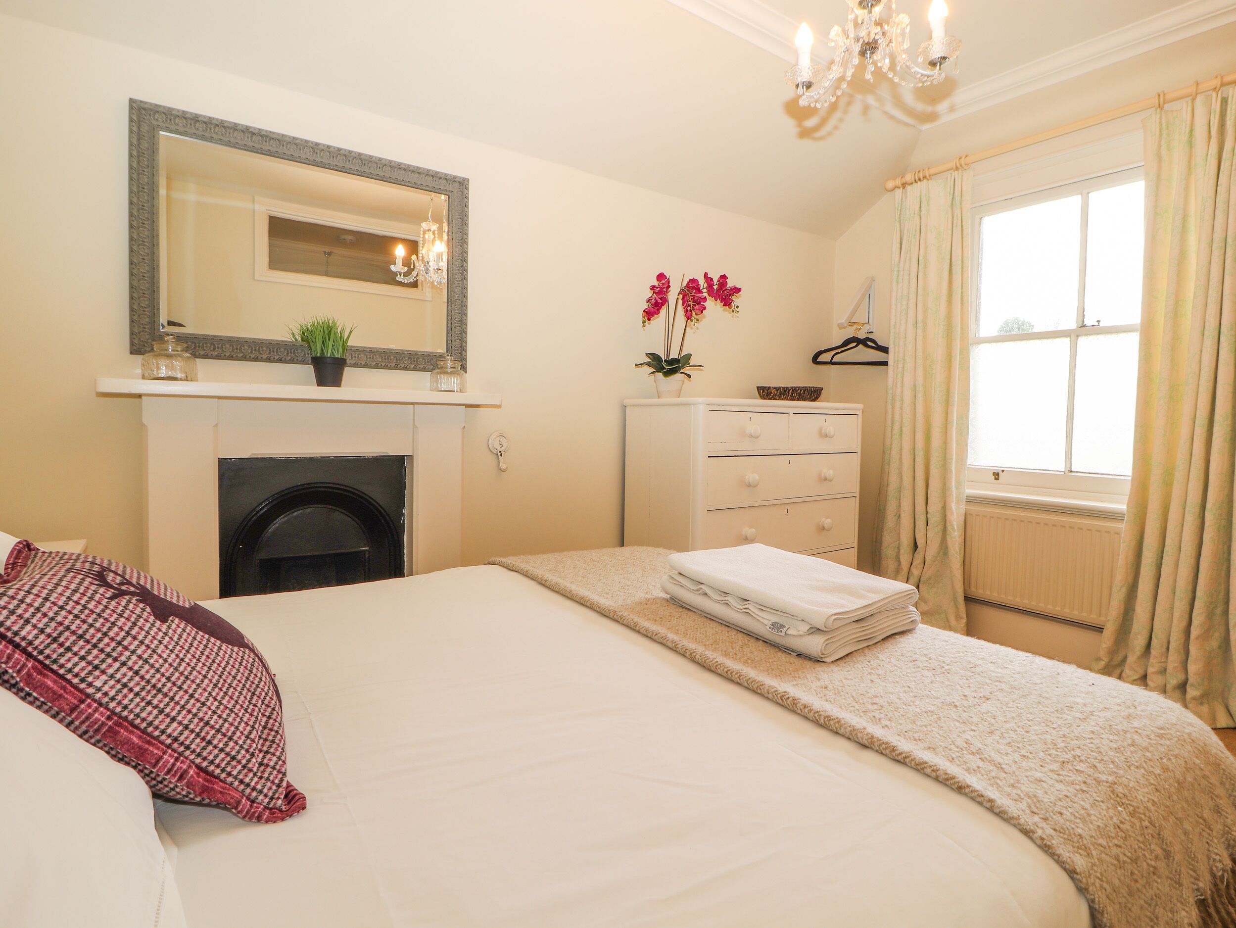 Une chambre à coucher comprenant un lit, une commode, un miroir, une cheminée et une fenêtre avec des rideaux.