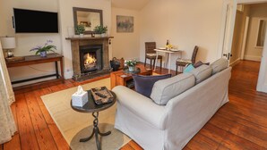 A living room with a fireplace, sofa, TV, and a dining area with chairs and a table. - Cook's Flat (Wrexham)