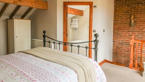 A bedroom with a bed, a wardrobe, a radiator, a brick wall, and a wooden staircase. - Barn Owl Cottage At Crook Hall Farm (Ormskirk)
