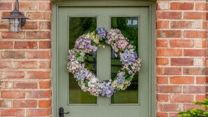 Een groene deur met een bloemenkrans en een lantaren aan de muur.