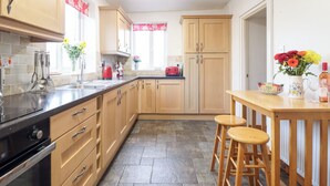 A modern kitchen with wooden cabinets, a black countertop, and a dining area with stools. - Bryn Re (Blaenau Ffestiniog)
