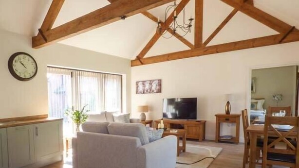A spacious living room with a large sofa, a television, and wooden beams on the ceiling. - Berringtons Barn (Market Drayton)