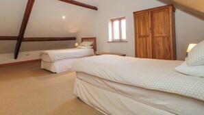 A bedroom with two beds, wooden beams, a window, and a wardrobe. - Riverside Barn (Abergavenny)