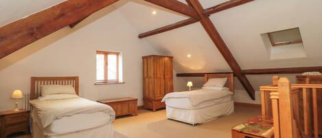 A bedroom with two beds, a wooden wardrobe, a small table, and a sloped ceiling with exposed beams.