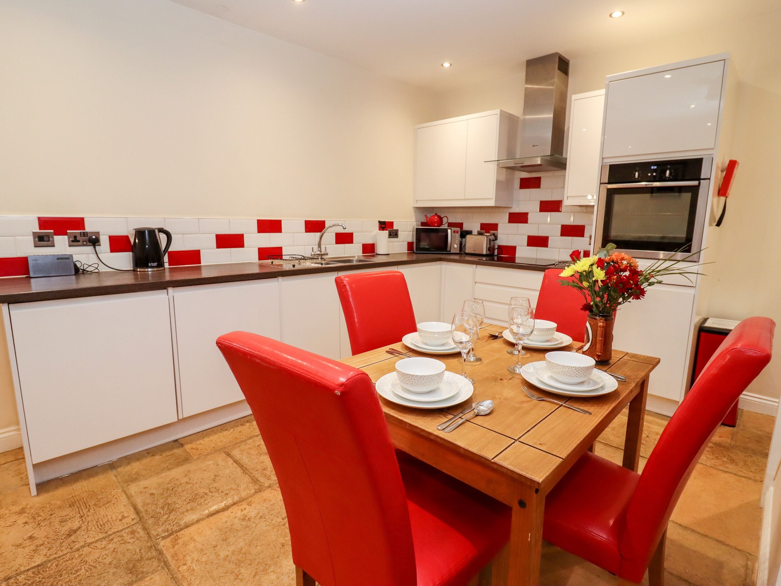 Une cuisine moderne avec des meubles blancs, un pare-feu rouge et blanc, et une table à manger pour quatre personnes, avec des chaises rouges.