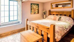 A bedroom with a wooden bed, a window, and a painting on the wall. - The Malthouse (Matlock)